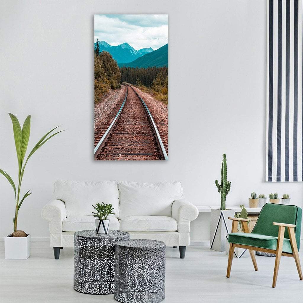 Railroad Tracks Curving Into Forest Vertical Canvas Wall Art in brown, green and blue, single vertical panel hung on a wall