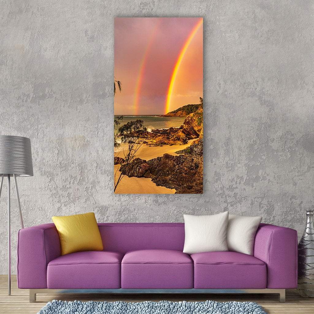 Sunset Double Rainbow Over Rocky Shore Vertical Canvas Wall Art in orange, yellow and pink, single vertical panel hung on a wall