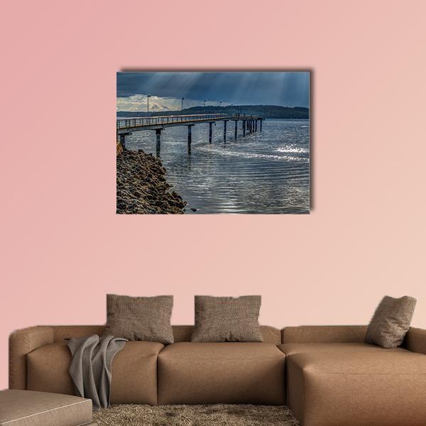 Sun Rays Over Pier and Rocky Shore Canvas Wall Art in gray and blue, single panel hung on a wall