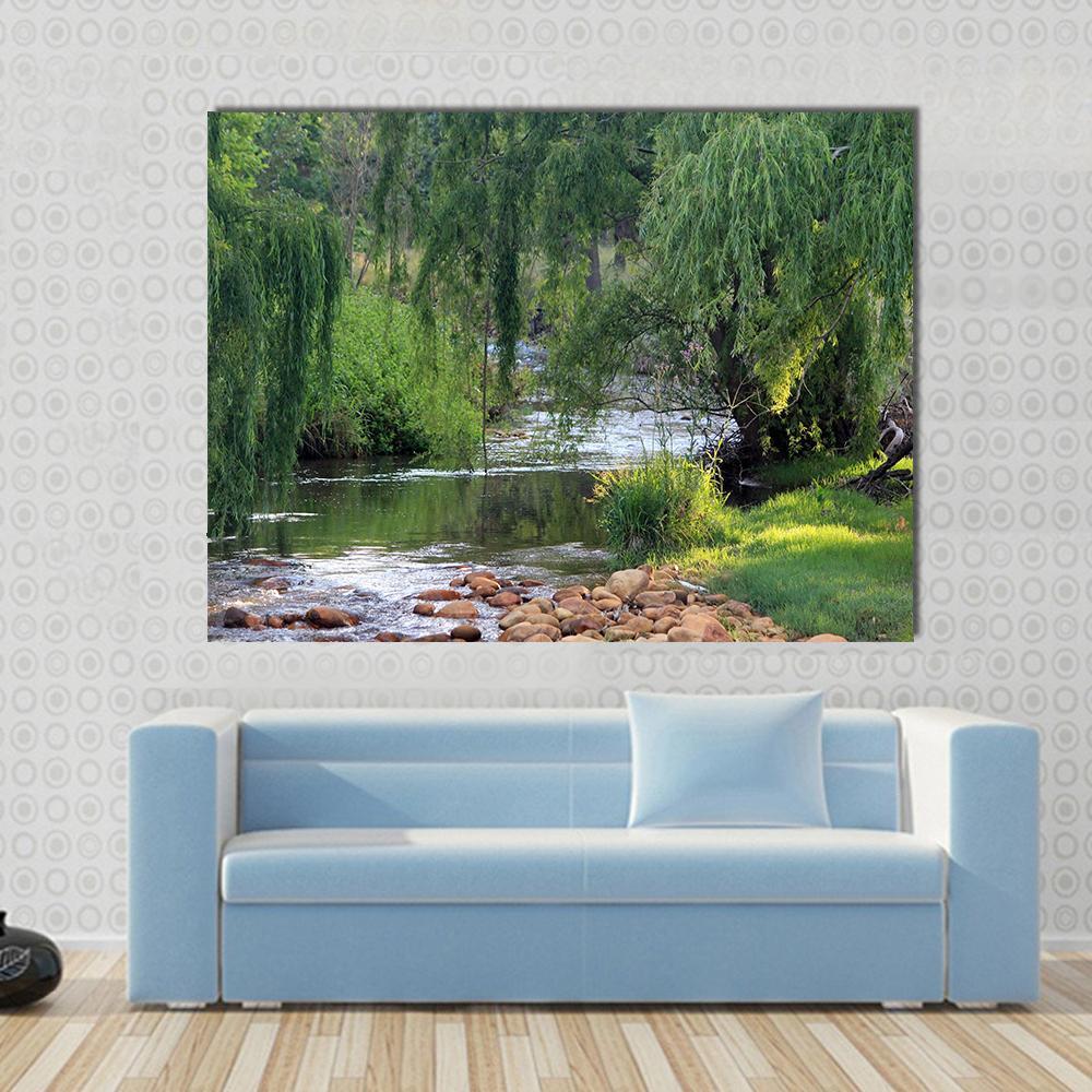 River Flowing Past Willow Trees Canvas Wall Art in brown and green, single panel hung on a wall