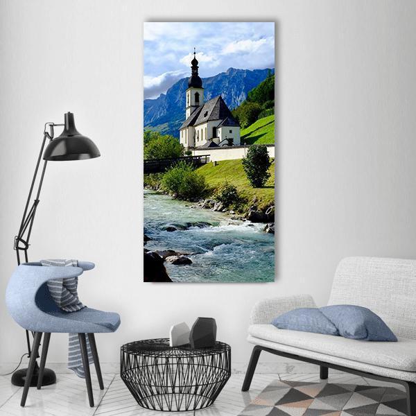 Berchtesgaden River with Church and Mountains Vertical Canvas Wall Art in white, green and blue, single vertical panel hung on a wall