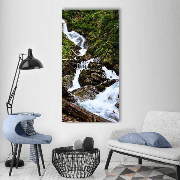 Waterfall Amid Wood Trunks and Boulders Vertical Canvas Wall Art in white, brown and green, single vertical panel hung on a wall