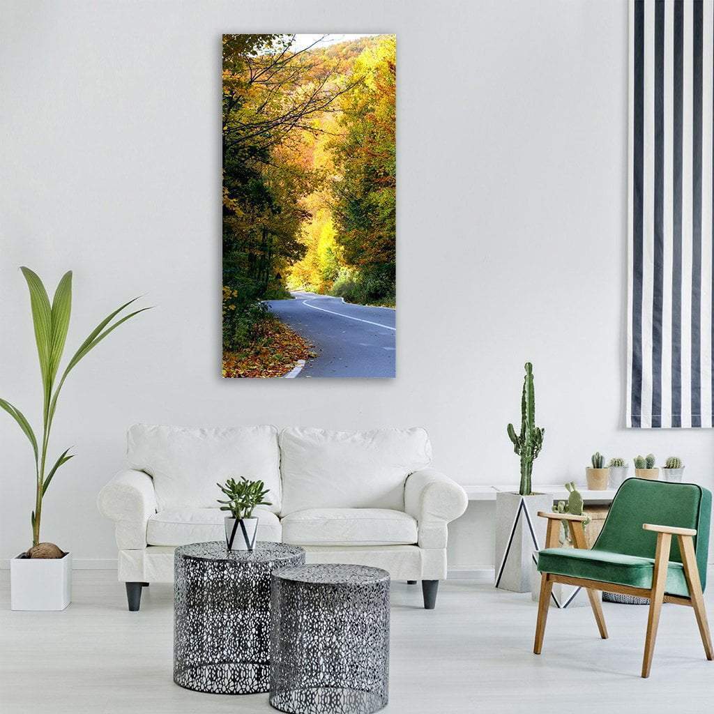 Curving Autumn Road in Mountain Forest Vertical Canvas Wall Art in orange, yellow and green, single vertical panel hung on a wall