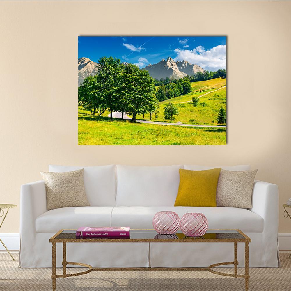 Winding Road Through Mountain Fields Canvas Wall Art in yellow, green and blue, single panel hung on a wall