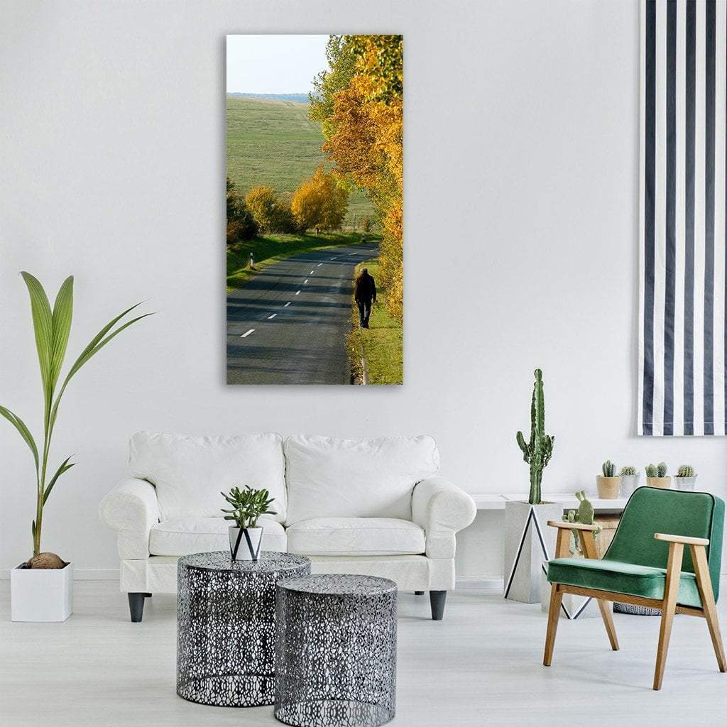 Person Walking on Tree-lined Autumn Road Vertical Canvas Wall Art in gray, yellow and green, single vertical panel hung on a wall