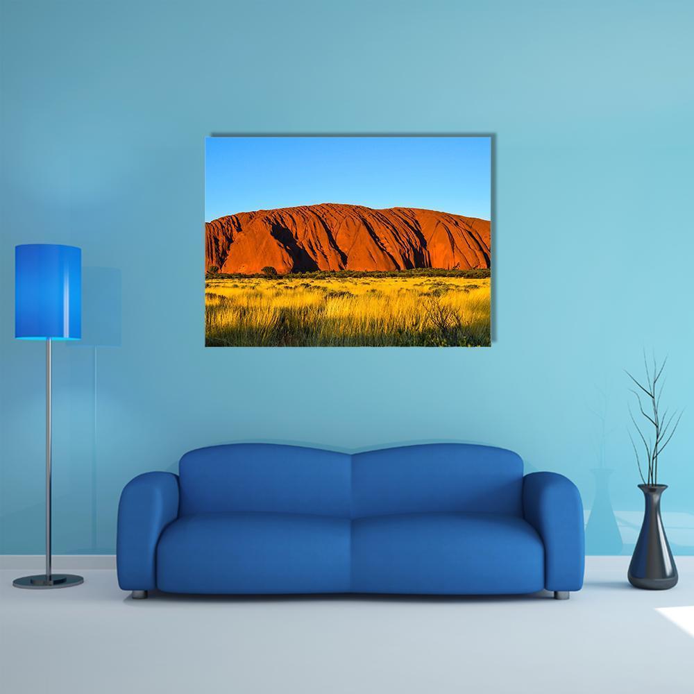 Uluru at Sunset Over Grassland Canvas Wall Art in orange, yellow and blue, single panel hung on a wall