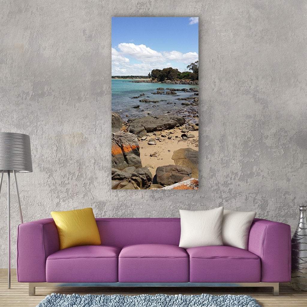 Rocky Beach Seascape with Calm Water Vertical Canvas Wall Art in beige, brown and blue, single vertical panel hung on a wall