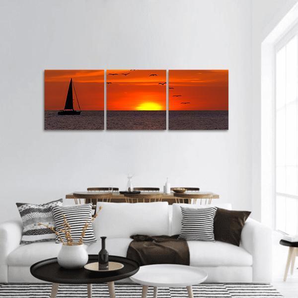 Sailboat at Sunset Panoramic Canvas Wall Art in black, orange and yellow, hung on a wall