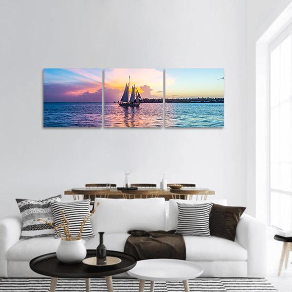 Two-masted Schooner at Sunset Panoramic Canvas Wall Art in orange, blue and purple, hung on a wall