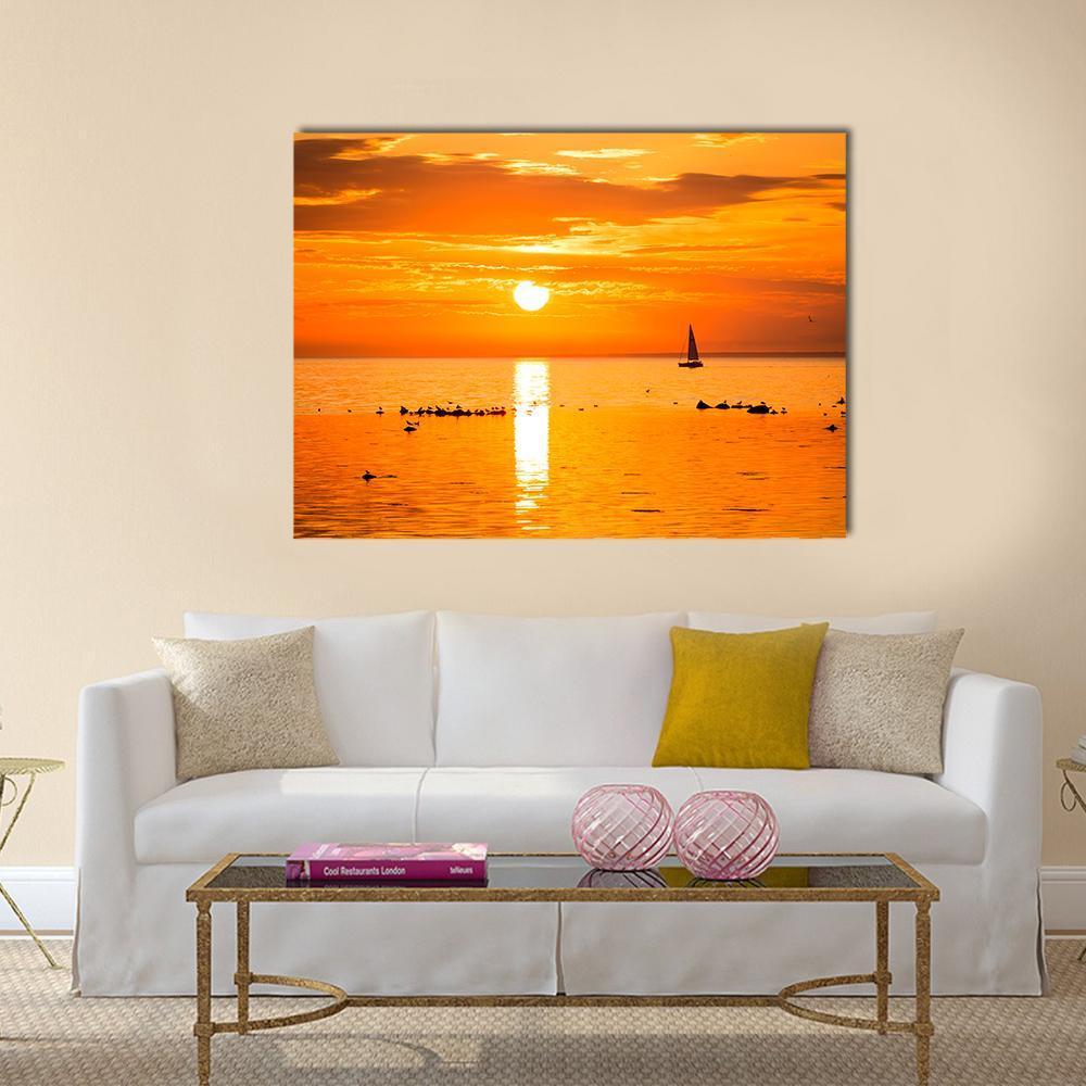 Sailboat at Sunset Over Ocean Canvas Wall Art in orange and yellow, single panel hung on a wall