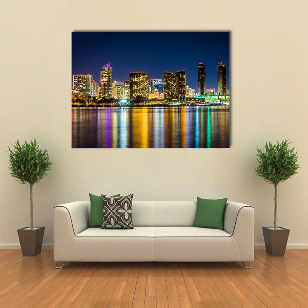 Night City Skyline with Water Reflections Canvas Wall Art in black, yellow and blue, single panel hung on a wall