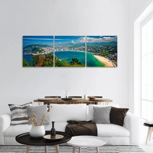 Coastal City Over Turquoise Bay Panoramic Canvas Wall Art in green and blue, hung on a wall