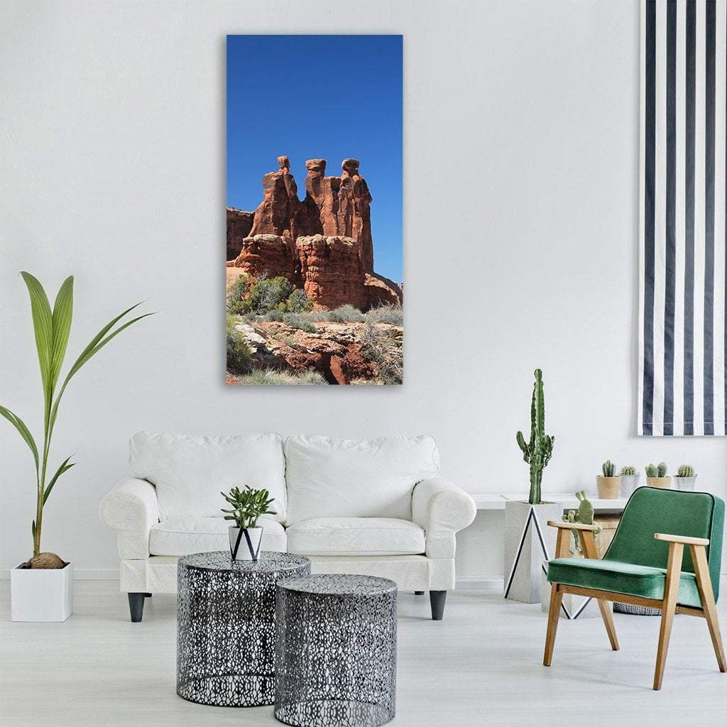 Three Sandstone Pinnacles Against Blue Sky Vertical Canvas Wall Art in brown, orange and blue, single vertical panel hung on a wall