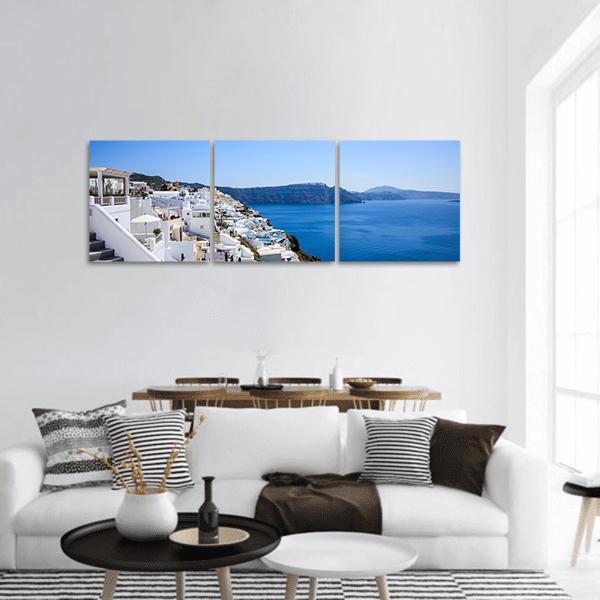 Santorini Cliffside Village Panoramic Canvas Wall Art in white and blue, hung on a wall