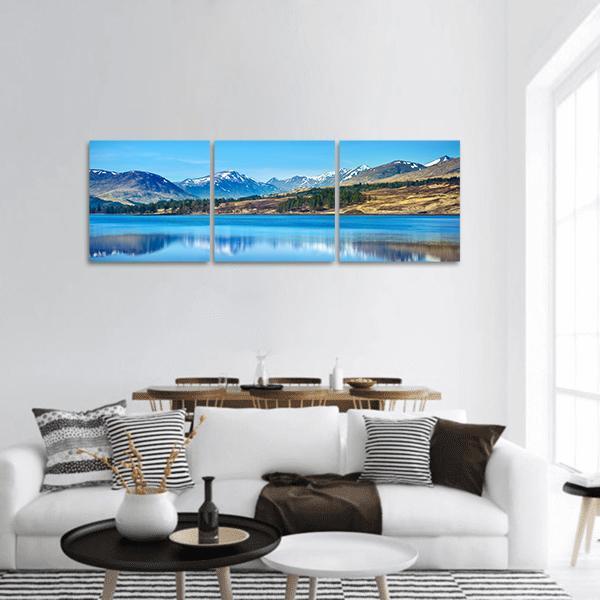 Scottish Highlands Lake Reflection Panoramic Canvas Wall Art in white, brown and blue, hung on a wall