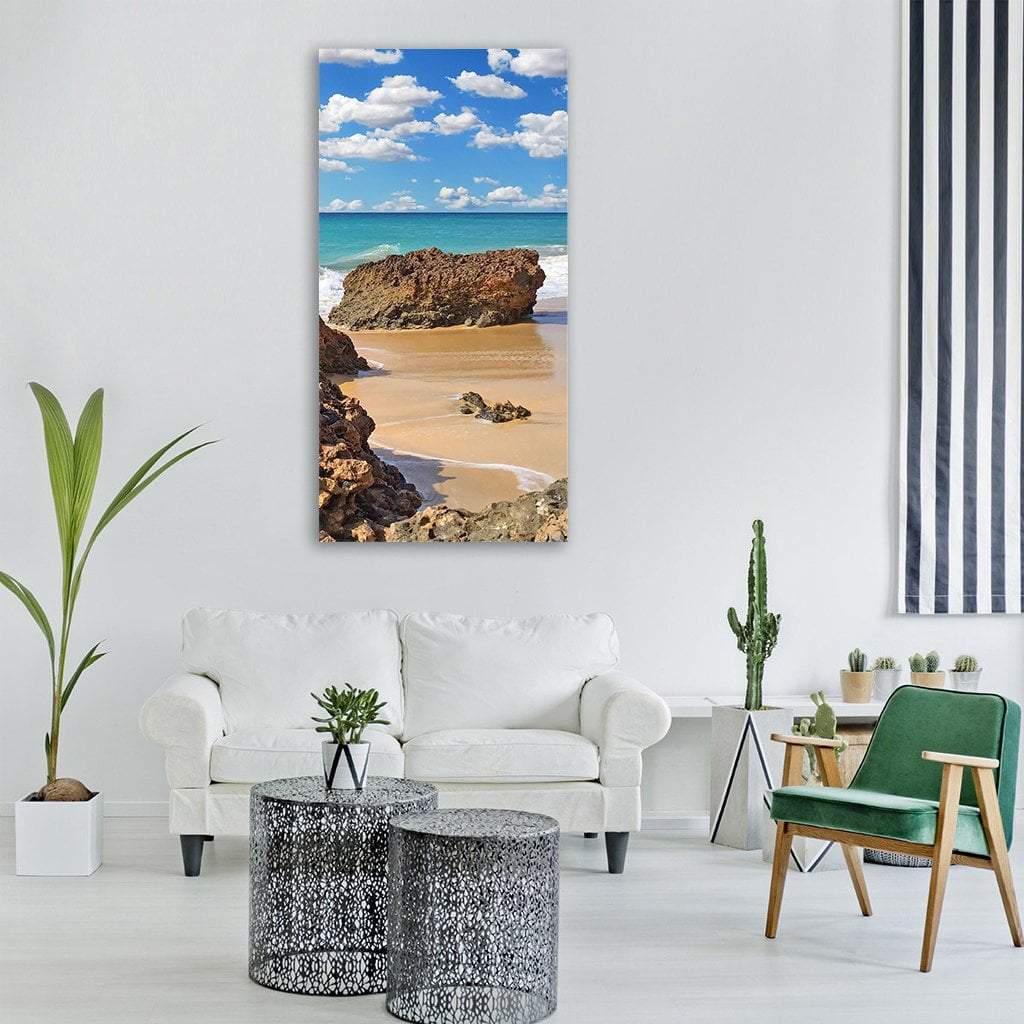 Weathered Rocks on Turquoise Beach Vertical Canvas Wall Art in beige, brown and blue, single vertical panel hung on a wall