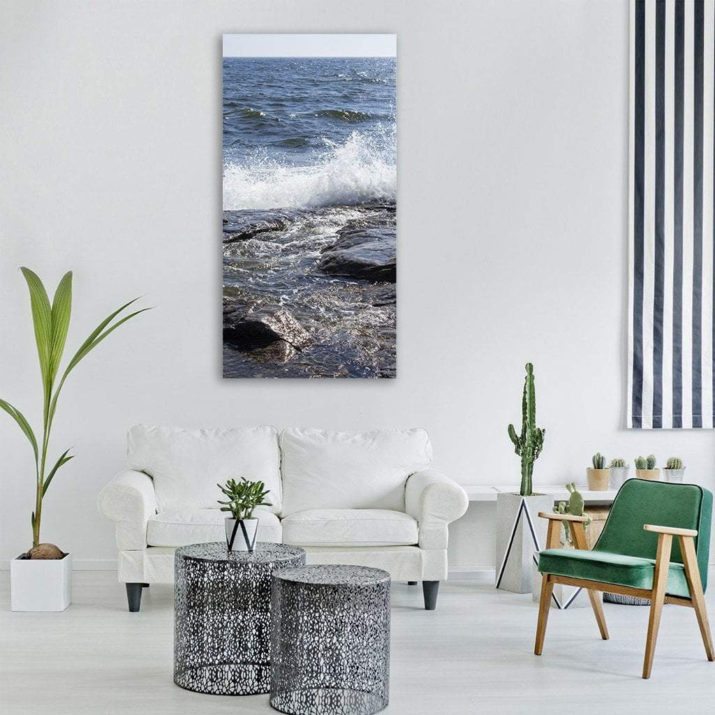 Crashing Wave Over Dark Coastal Rocks Vertical Canvas Wall Art in white, gray and blue, single vertical panel hung on a wall