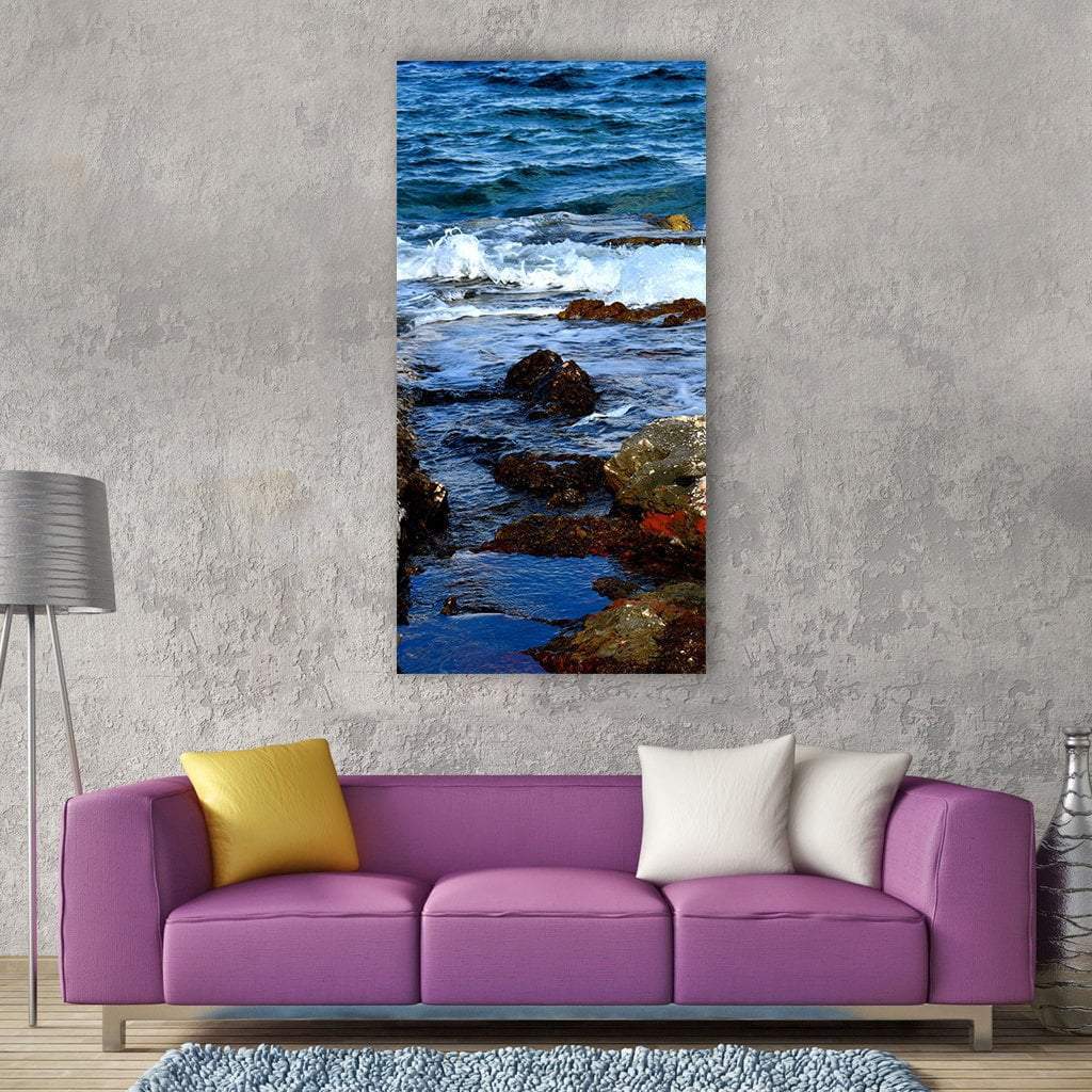 Blue Ocean Wave Crashing on Rocks Vertical Canvas Wall Art in white, brown and blue, single vertical panel hung on a wall