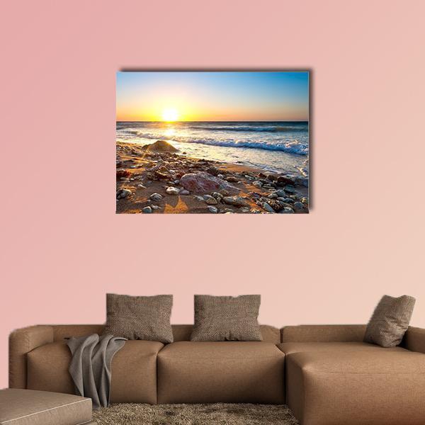 Sunset Seascape with Pebble Shore Canvas Wall Art in orange, yellow and blue, single panel hung on a wall