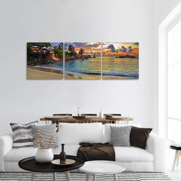 Tropical Beach Cafe at Sunset Panoramic Canvas Wall Art in orange, yellow and blue, hung on a wall