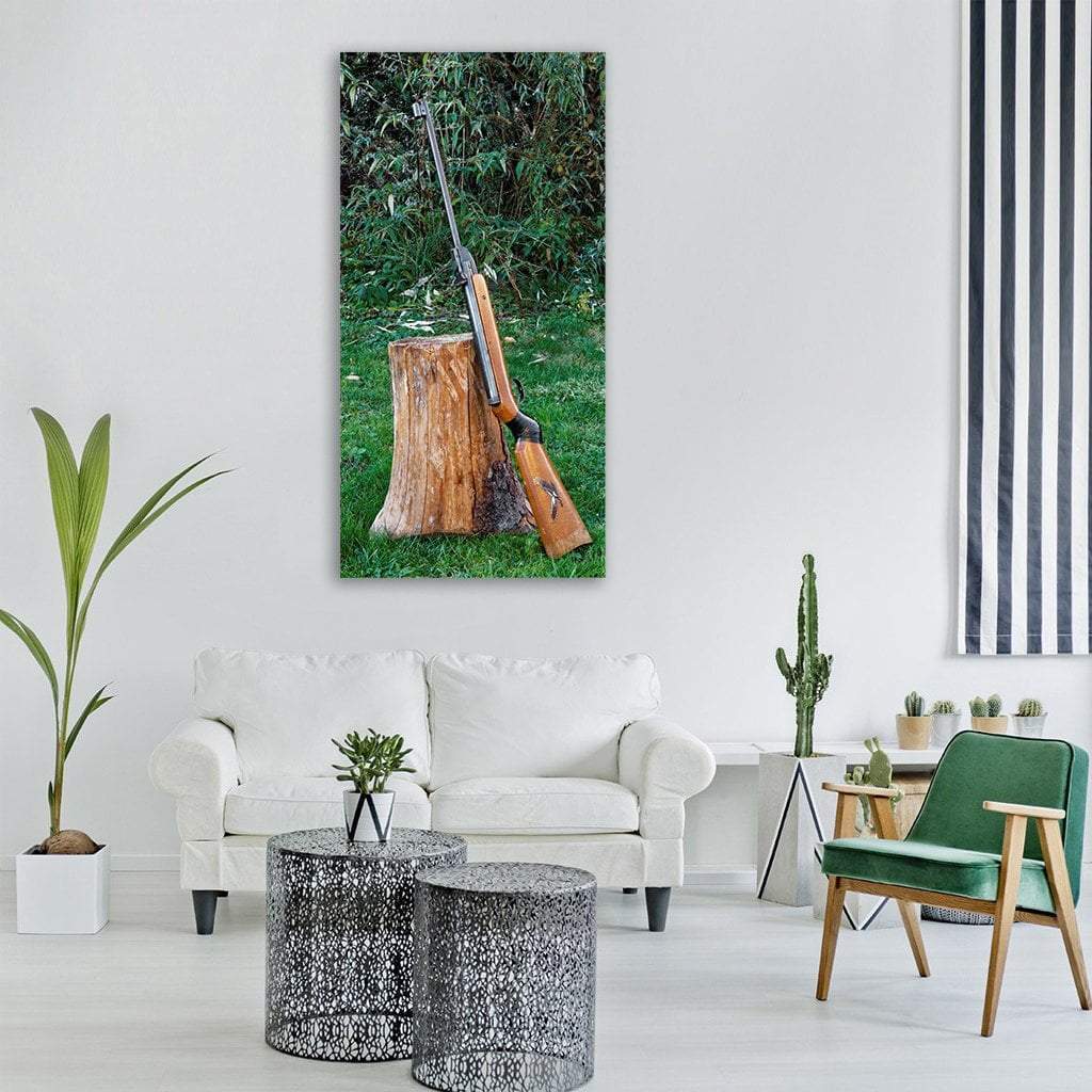 Wooden Rifle on Tree Stump Vertical Canvas Wall Art in brown and green, single vertical panel hung on a wall