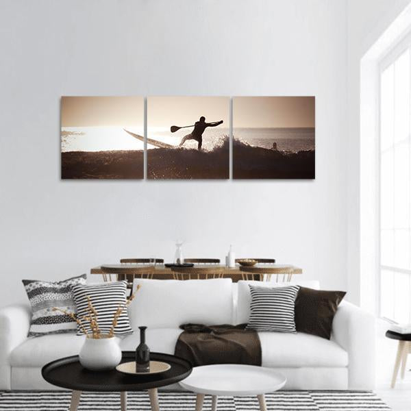 Paddleboarder Silhouette on Ocean Wave Panoramic Canvas Wall Art in black, beige and brown, hung on a wall