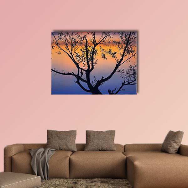 Tree Silhouette at Sunrise Canvas Wall Art in black, orange and blue, single panel hung on a wall