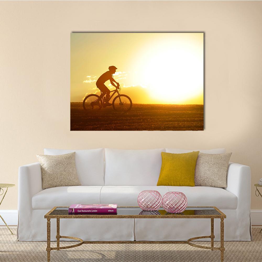 Cyclist Silhouette at Sunset Canvas Wall Art in black, orange and yellow, single panel hung on a wall