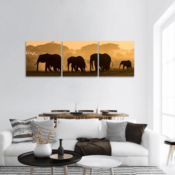 Elephant Silhouettes at Golden Hour Panoramic Canvas Wall Art in black, orange and yellow, hung on a wall