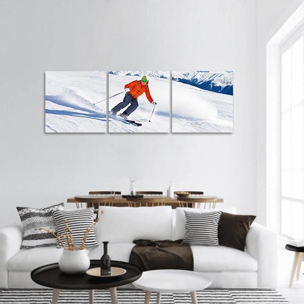 Masked Skier on Snowy Mountain Slope Panoramic Canvas Wall Art in white, orange and blue, hung on a wall