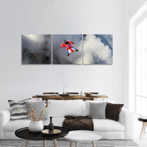 Wingsuit Flyer Over Jagged Mountain Peaks Panoramic Canvas Wall Art in white, gray and blue, hung on a wall