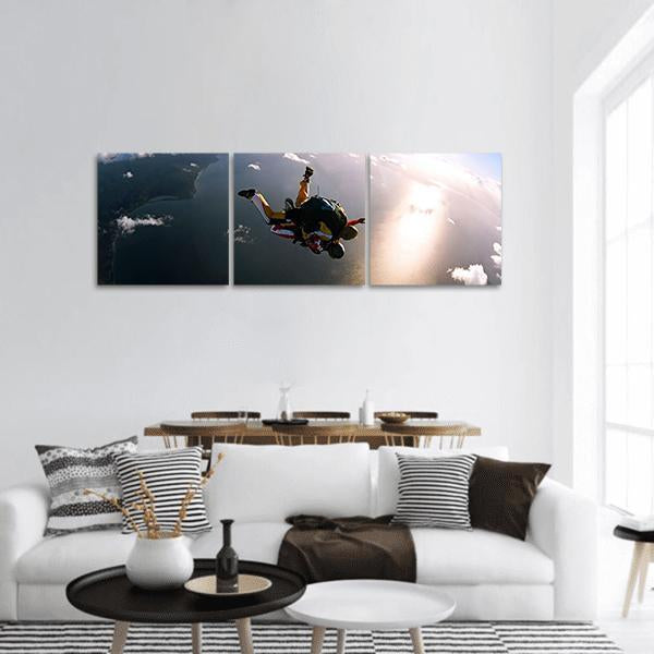 Tandem Skydivers Over Sunlit Coastline Panoramic Canvas Wall Art in black, white and blue, hung on a wall