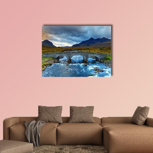 Arched Stone Bridge Beneath Stormy Mountain Sky Canvas Wall Art in gray, brown and blue, single panel hung on a wall