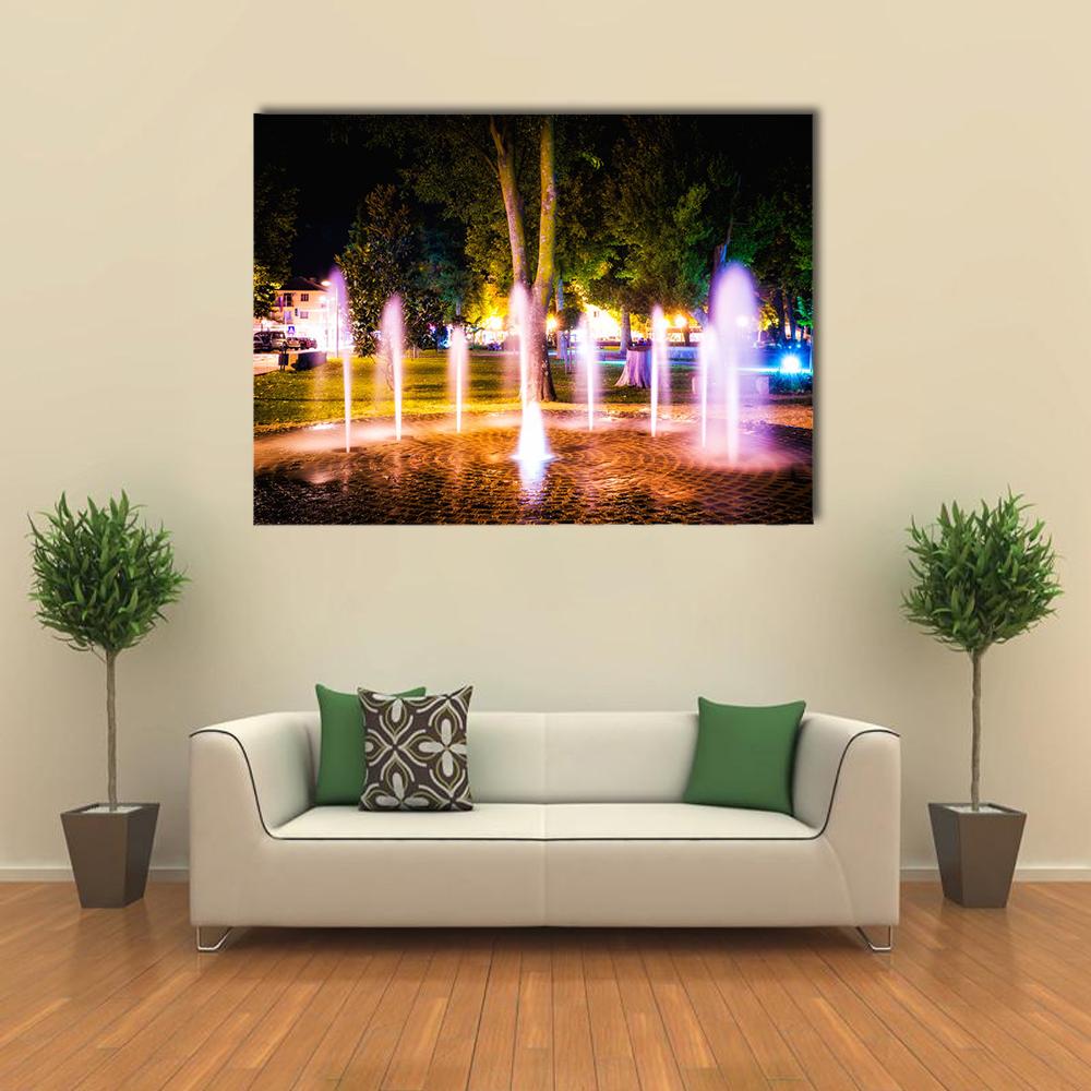 Summer Night Illuminated Fountain Canvas Wall Art in black, yellow and purple, single panel hung on a wall