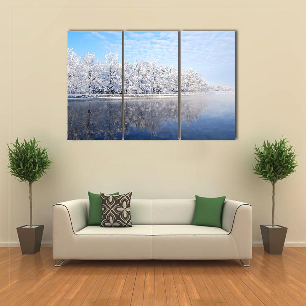 Snow-covered Trees Reflecting on Icy Water Canvas Wall Art in white and blue, 3 panel horizontal set hung on a wall