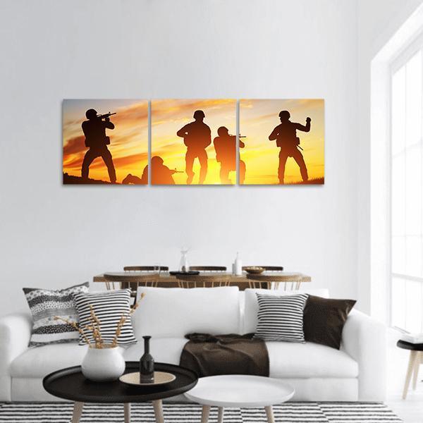 Soldier Silhouettes at Golden Sunset Panoramic Canvas Wall Art in black, orange and yellow, hung on a wall