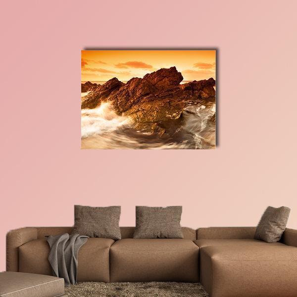 Sunset Waves Crashing on Rocky Shore Canvas Wall Art in brown, orange and yellow, single panel hung on a wall