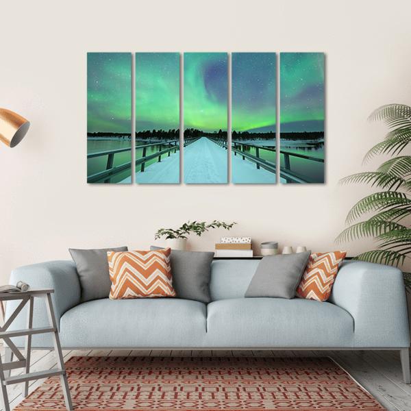 Northern Lights Over Snowy Bridge and River Canvas Wall Art in white, green and blue, hung on a wall