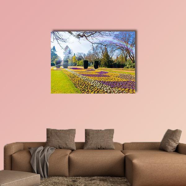 Spring Garden with Sunlit Flower Bed Canvas Wall Art in yellow, green and purple, single panel hung on a wall