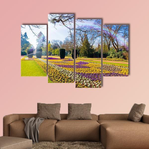 Spring Garden with Sunlit Flower Bed Canvas Wall Art in yellow, green and purple, 3 panel horizontal set hung on a wall