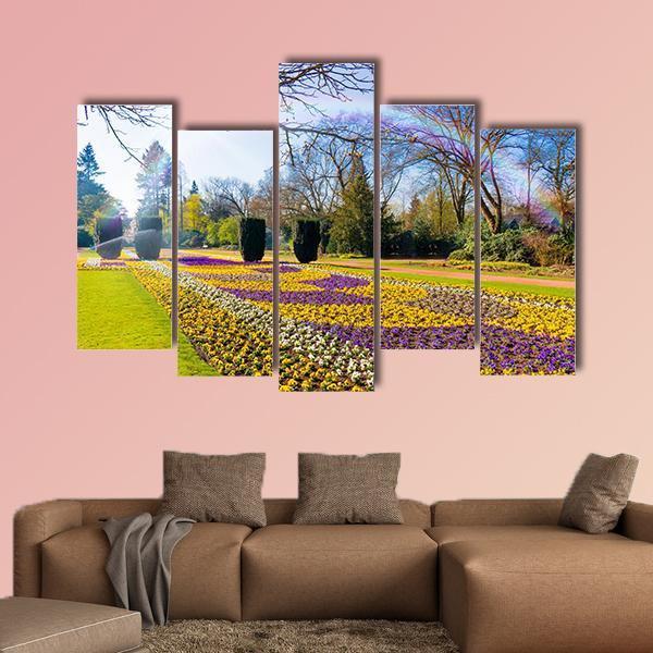 Spring Garden with Sunlit Flower Bed Canvas Wall Art in yellow, green and purple, 3 panel horizontal set hung on a wall