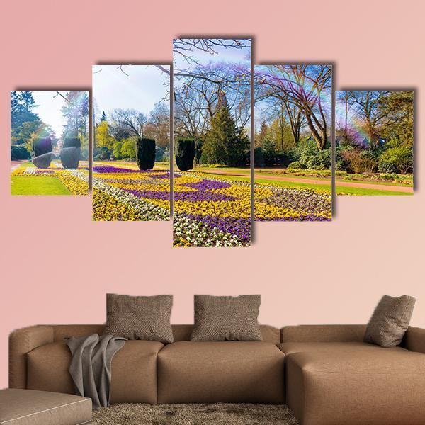 Spring Garden with Sunlit Flower Bed Canvas Wall Art in yellow, green and purple, 3 panel horizontal set hung on a wall