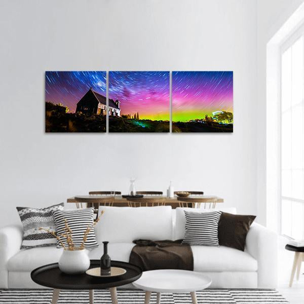Stone Chapel Under Aurora and Star Trails Panoramic Canvas Wall Art in green, blue and purple, hung on a wall