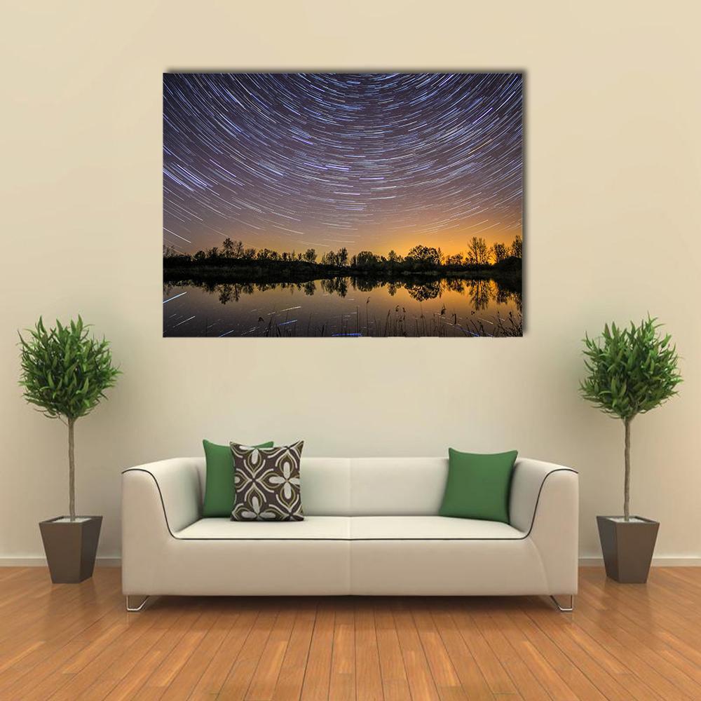 Star Trails Over Reflective Lake Canvas Wall Art in black, orange and blue, single panel hung on a wall