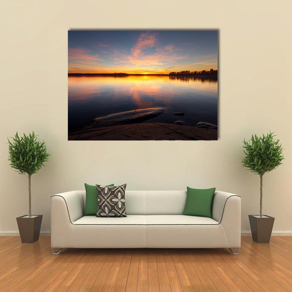 Sunrise Over Still Sea and Rocky Shore Canvas Wall Art in orange, yellow and blue, single panel hung on a wall