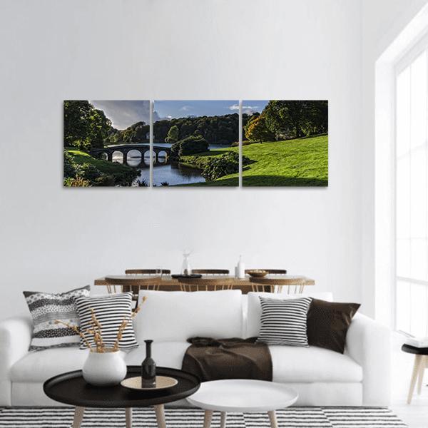 Multi-arch Stone Bridge with River Reflections Panoramic Canvas Wall Art in gray, green and blue, hung on a wall