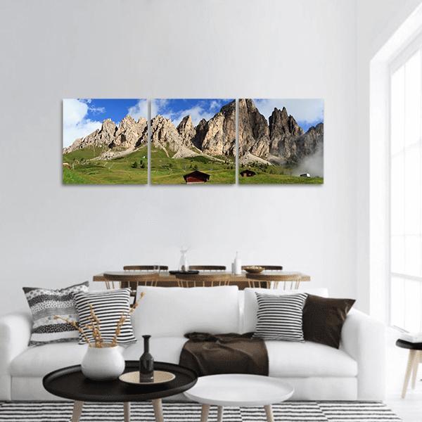 Sunlit Alpine Mountains with Wooden Huts Panoramic Canvas Wall Art in gray, green and blue, hung on a wall