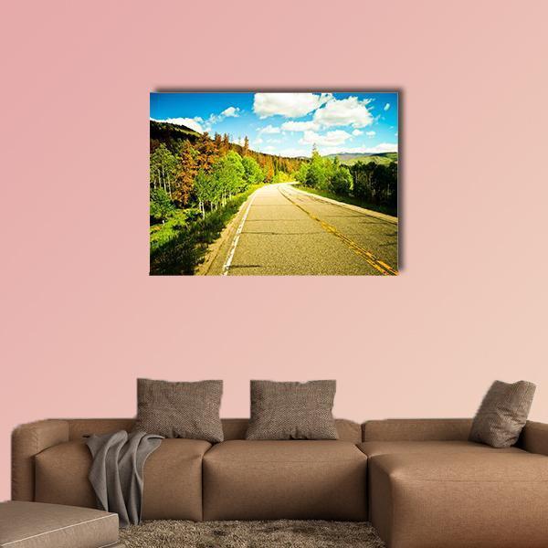 Sunny Road Among Colorful Trees Canvas Wall Art in yellow, green and blue, single panel hung on a wall
