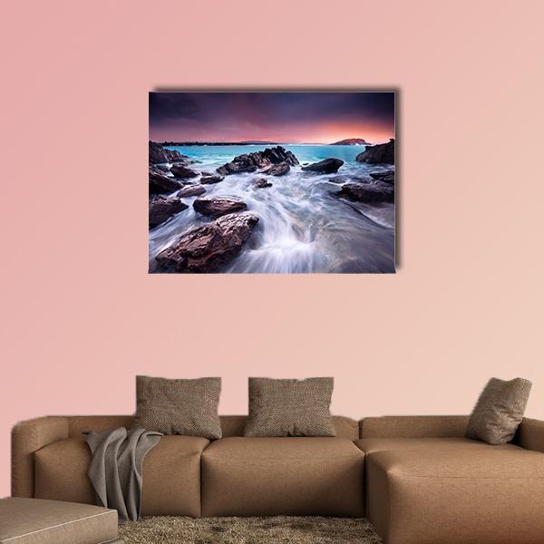 Sunset Over Rocky Coastline with Distant Island Canvas Wall Art in orange, blue and purple, single panel hung on a wall