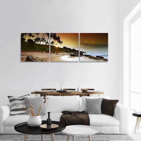 Sunset Over Coconut Palms on Beach Panoramic Canvas Wall Art in brown, orange and yellow, hung on a wall